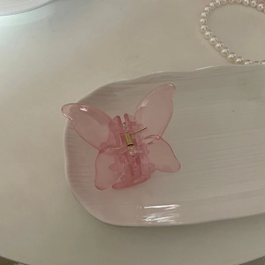 Pince à cheveux papillon en acrylique rose translucide sur un plateau à bijoux blanc