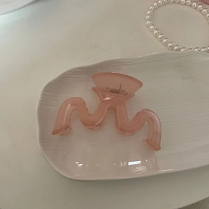 Pince à cheveux ondulée rose élégante en acrylique sur un plateau à bijoux en céramique
