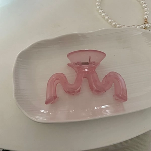 Vue détaillée d'une pince à cheveux ondulée en acrylique rose sur une assiette blanche