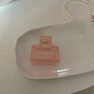 Détail d'une pince à cheveux rectangulaire rose translucide avec ressort sur plaque blanche