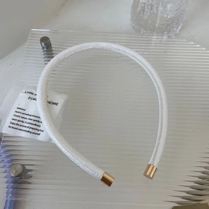 Détail d'un serre-tête blanc en satin avec embouts dorés sur support acrylique texturé