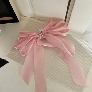 Détail d'une grande barrette à nœud en tulle rose avec perles blanches sur verre