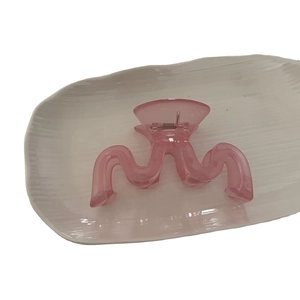 Pince à cheveux rose translucide forme vague géométrique sur un plateau blanc