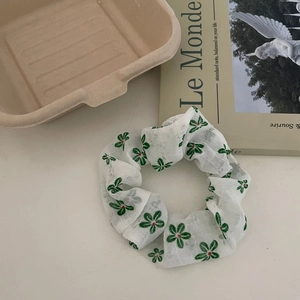 Gros plan sur un chouchou en organza blanc avec motifs floraux verts et texture plissée