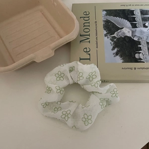 Détail d'un chouchou en mousseline blanche avec motifs floraux verts et magazine français