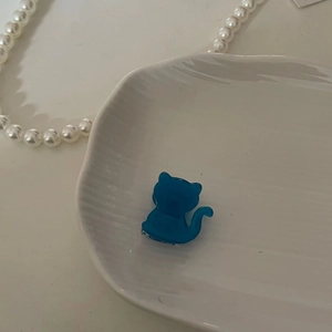 Pinza para el pelo azul con forma de gato hecha de acetato en un plato de cerámica blanca