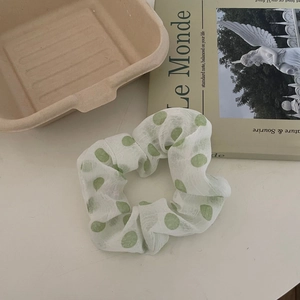 Détail du tissu en maille légère et des pois verts sur le chouchou blanc pour cheveux