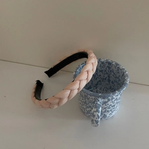 Pink braided headband with glossy finish on a decorative blue and white ceramic cup