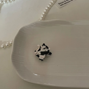 Detalle de una mini pinza para el pelo de acetato con forma de gato sobre una bandeja de porcelana