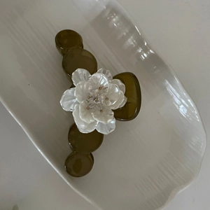 French style olive green hair claw clip with a white floral ornament on a ceramic tray