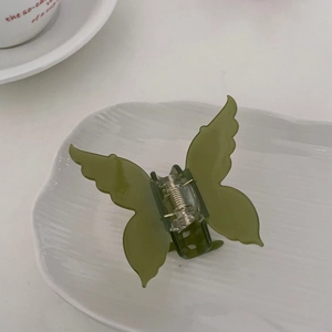 Détail d'une pince à cheveux papillon vert olive avec ressort argenté sur un plateau blanc