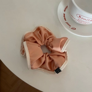 French style satin organza hair scrunchie in pink with cream trim on a desk