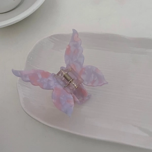 Détail d'une pince à cheveux papillon en acétate violet et rose sur un plateau blanc