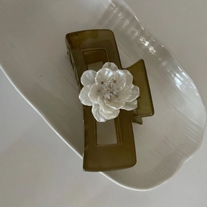 Detail of square brown claw clip with 3D white flower on a white ceramic tray