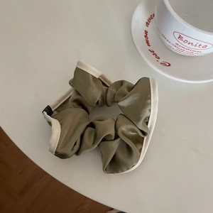 Detail of olive green satin scrunchie with beige piping and branded woven label