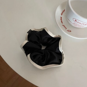 Close-up of elegant black satin scrunchie with cream wavy edge and woven label