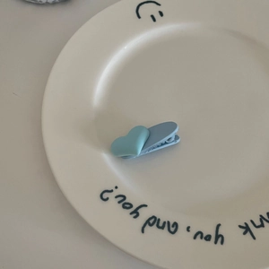 Detail einer blauen herzförmigen Haarklammer auf weißem Keramikteller mit Smileys