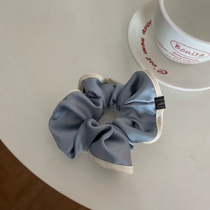 Close-up of a blue-grey satin scrunchie with cream piping and a small brand label