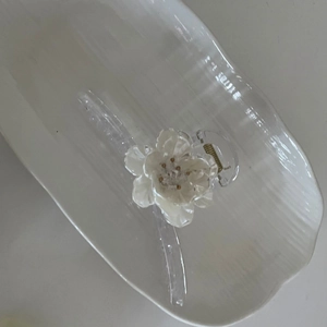 Detail view of a white 3D flower hair claw clip with golden stamen on a ceramic tray
