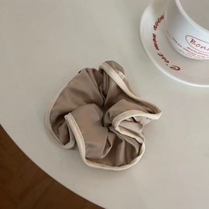 Detail of champagne satin scrunchie with cream trim on a white decorative setting