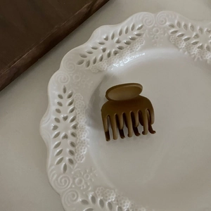 Détail d'une pince à cheveux mate marron posée sur une assiette décorative en porcelaine