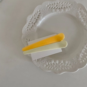 Detail von gelben und beigen matten Macaron-Haarspangen auf weißem Porzellan
