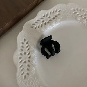 Vue détaillée d'une petite pince à cheveux noire mate sur une plaque en céramique