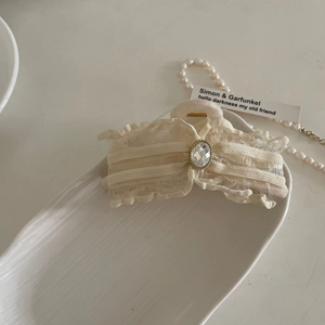 Elegant cream mesh bow hair claw clip with oval crystal gemstone on a ceramic tray