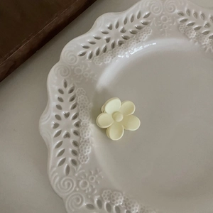 Gros plan d'une pince à cheveux fleur crème mate sur un plateau en céramique