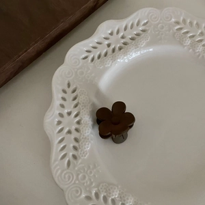 Gros plan d'une pince à cheveux fleur mate marron foncé sur une assiette en céramique