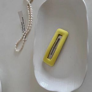 Rectangular bright yellow fabric sponge hair clip on a white decorative ceramic tray