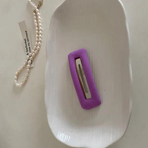 Detailed view of a purple rectangular velvet hair clip with a silver metal base on a tray
