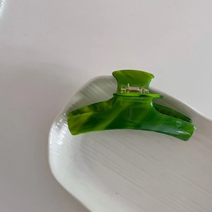Pince à cheveux élégante en acétate à texture marbre vert sur un plateau blanc