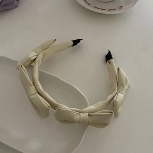 Detailed top view of cream satin headband with four bows and protective black tips