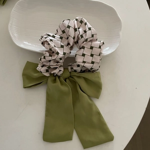 Detail of green plaid scrunchie with a large fabric bow on a white ceramic plate
