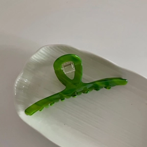 Pince à cheveux en acétate vert texturé sur plateau en céramique blanche pour coiffure