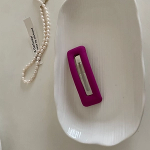 Detail view of a rose purple matte rectangular hair clip on a white ceramic tray