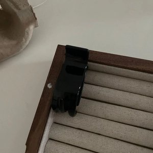 Petite pince à cheveux triangulaire noire brillante sur un plateau à bijoux en bois