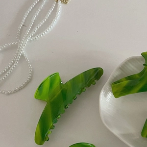 Gros plan d'une pince à cheveux en acétate vert marbré sur une assiette en céramique blanche