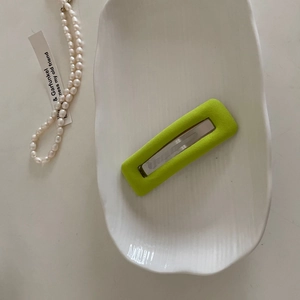 Detail of neon green matte snap hair clip with silver metal bar on white tray
