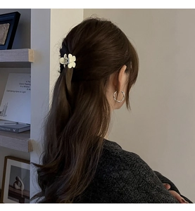 Gros plan d'une pince à cheveux fleur blanche et de créoles argentées sur un modèle