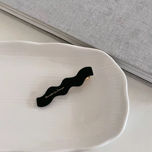 Elegante pinza de pelo ondulada negra de acrílico con letras doradas en plato cerámico