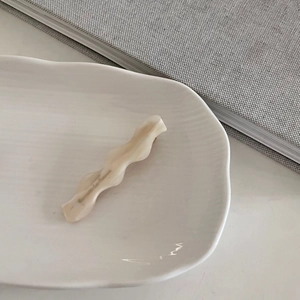 Pinza para el pelo ondulada de acrílico crema con textura de mármol en plato de cerámica