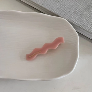 Detalle de pinza de pelo ondulada rosa en acrílico con letras doradas en bandeja blanca