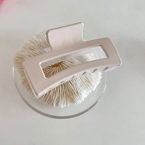 Macro detail of cream-colored square geometric hair claw clip on elegant white pedestal