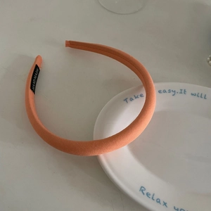 Dettaglio di un cerchietto arancione fatto a mano con etichetta nera cucita internamente