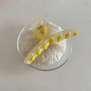 Detail of yellow translucent hair claw clip with cross design on white coral display