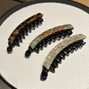 Three acetate banana hair clips in tortoiseshell and marble patterns on white tray