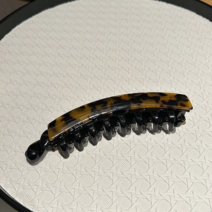 Classic tortoiseshell banana hair clip with amber pattern and black resin comb teeth