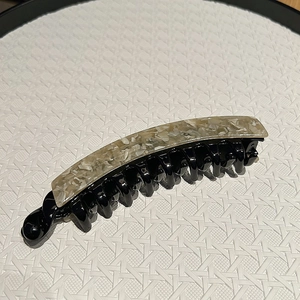 Detail of banana hair clip with elegant beige marble pattern and smooth black base